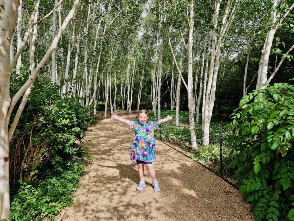 Young girl wearing a bright dress, stood with her hands up, on a pathway at Anglesey Abbey