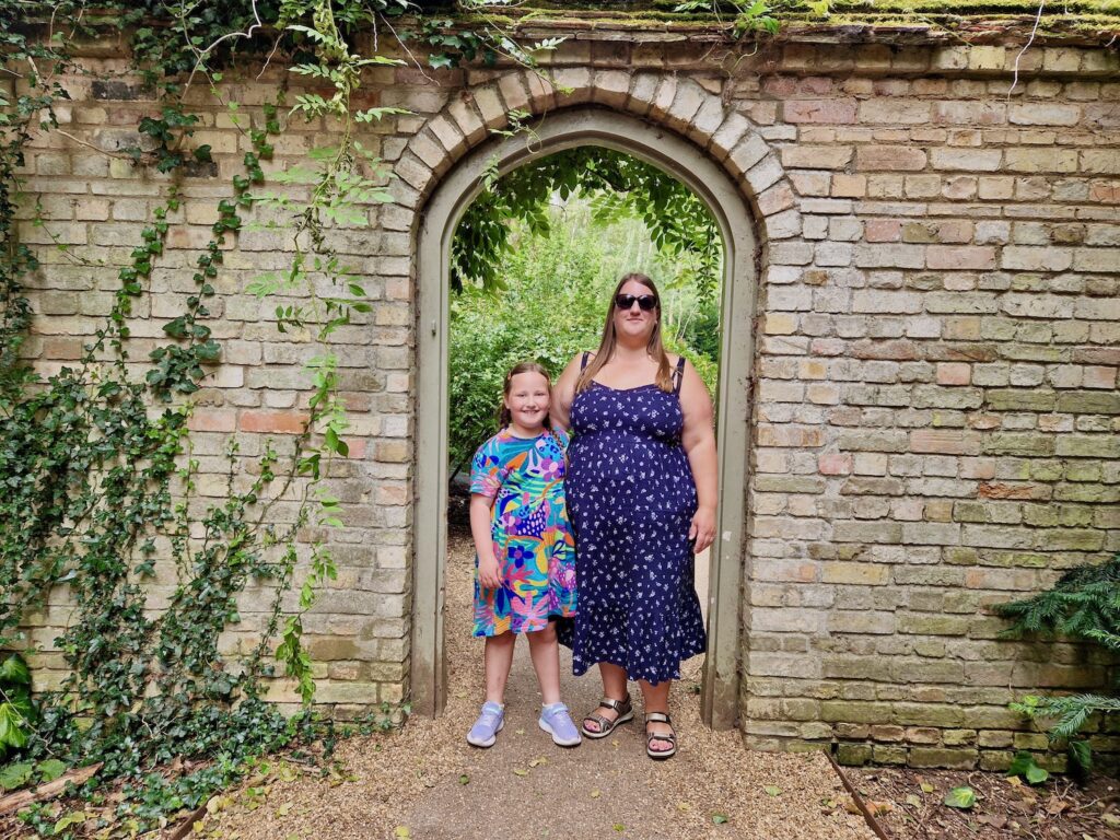 Mother and daughter, both wearing summer dresses, stood in a stone archway at Anglesey Abbey