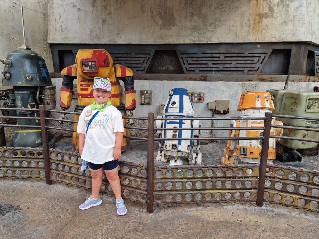 Erin stood in front of droids in Galaxy's Edge at Hollywood Studios. She is wearing a hat and a cooling towel around her neck