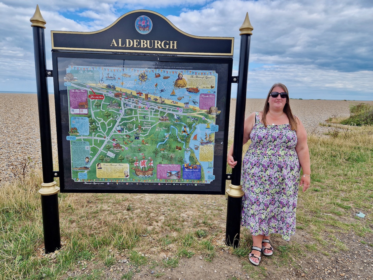 Myself, a 36 year old woman in a purple strappy dress, stood next to the Aldeburgh map