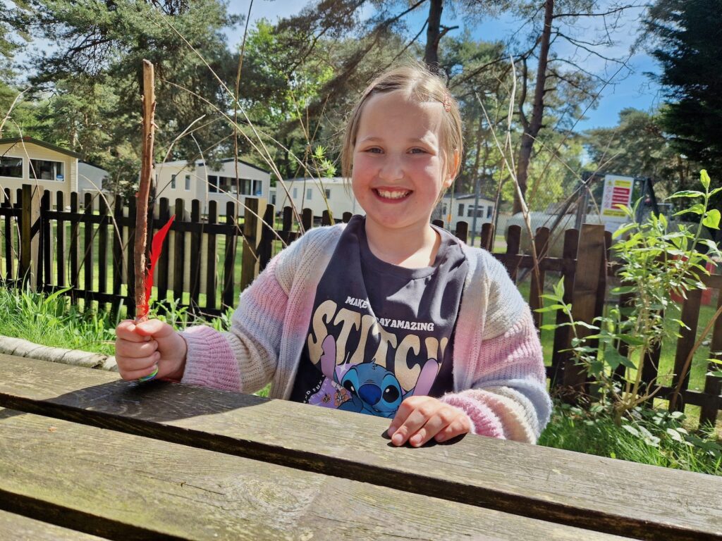 An 8 year old girl wearing a bright cardigan and a Lilo and Stitch t-shirt, holding a wand made from a stick 