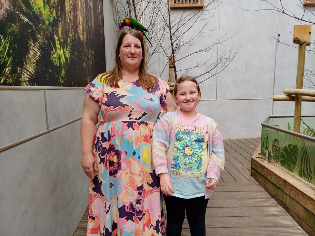 Mother and daughter in the Australian Rainbow exhibit at Colchester Zoo. The mother has a lorikeet sat on top of her head. 