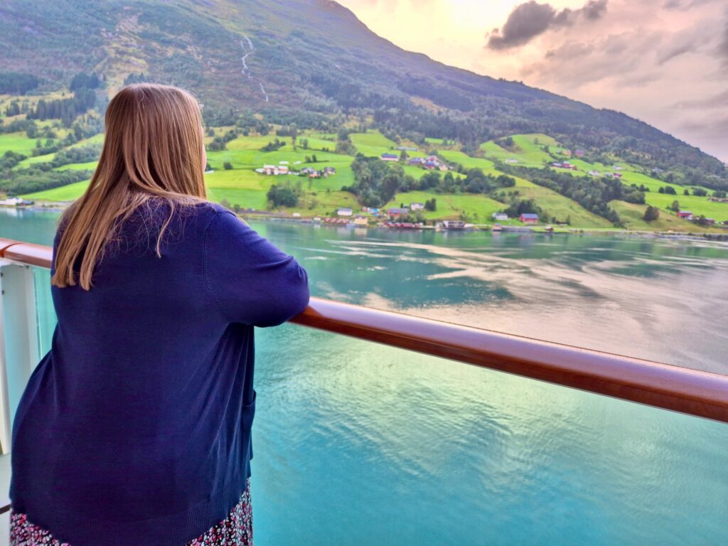 Lyndsey, a 38 year old woman wearing a long dress and cardigan, looking out on a chilly morning on the Norwegian Fjords