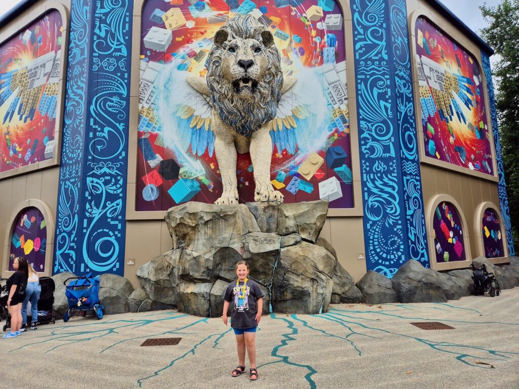 8 year old girl in a bright green floral dress and sunglasses, standing outside Flight of the Sky Lion at Legoland Windsor