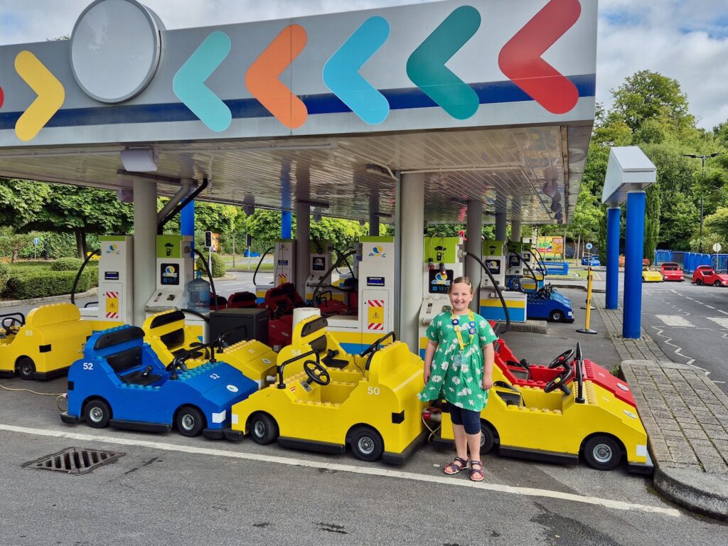 Erin, an 8 year old girl in a bright green floral dress and navy leggings, stood with a car at Lego City Driving School