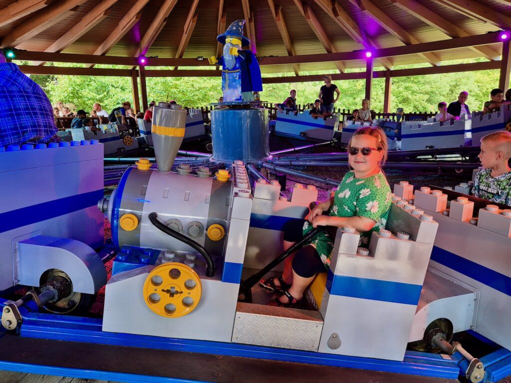 8 year old girl in a bright green floral dress and sunglasses, riding Merlin’s Apprentice at Legoland Windsor