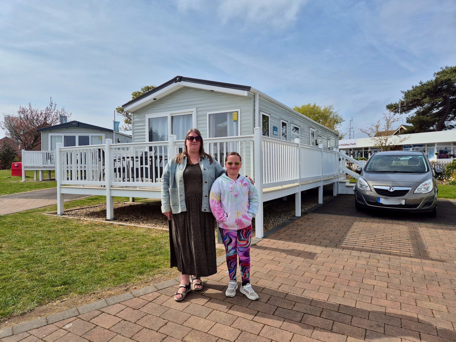 Mum and daughter standing outside a white caravan with decking at Haven Caister-on-Sea, with a parked car to the side.