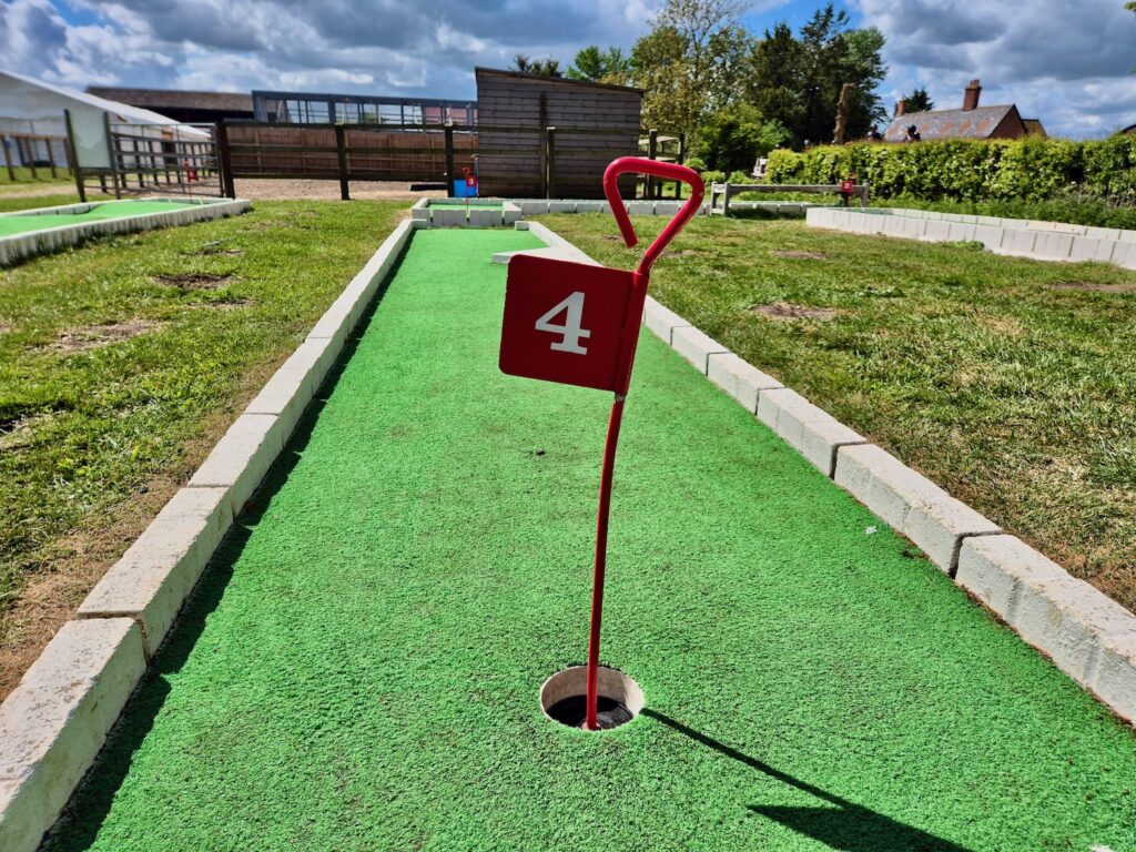 Mini golf hole number 4 with a red flag on a bright green course at Camel Park Oasis in Suffolk.