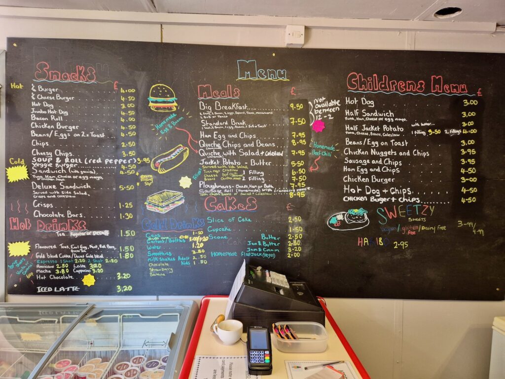 Café menu board at Camel Park Oasis showing a variety of snacks, meals, drinks, and children’s food options.