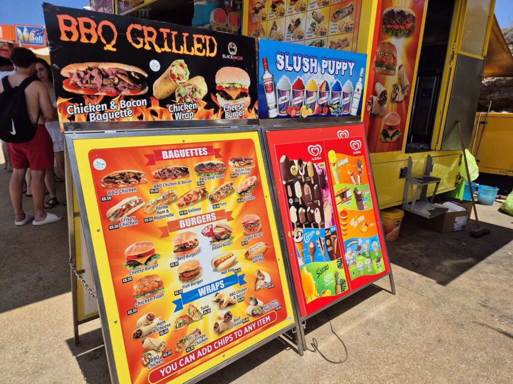 Colourful food stall menu offering BBQ grilled baguettes, burgers, wraps, and ice creams near the Blue Lagoon in Malta