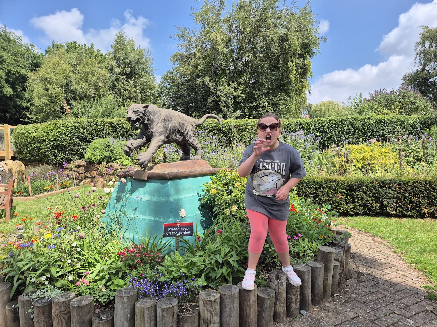 Child posing like a tiger in front of a tiger statue surrounded by colourful flowers