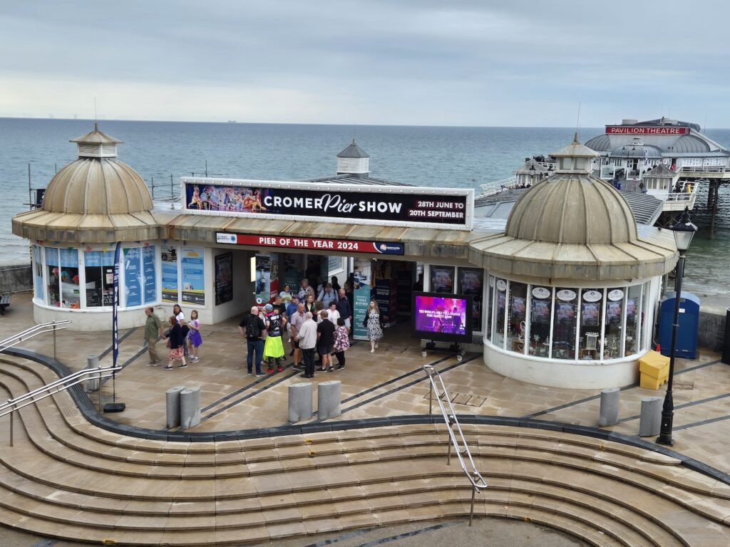 Exterior of Cromer Pier Pavilion Theatre with people gathered outside under a cloudy sky