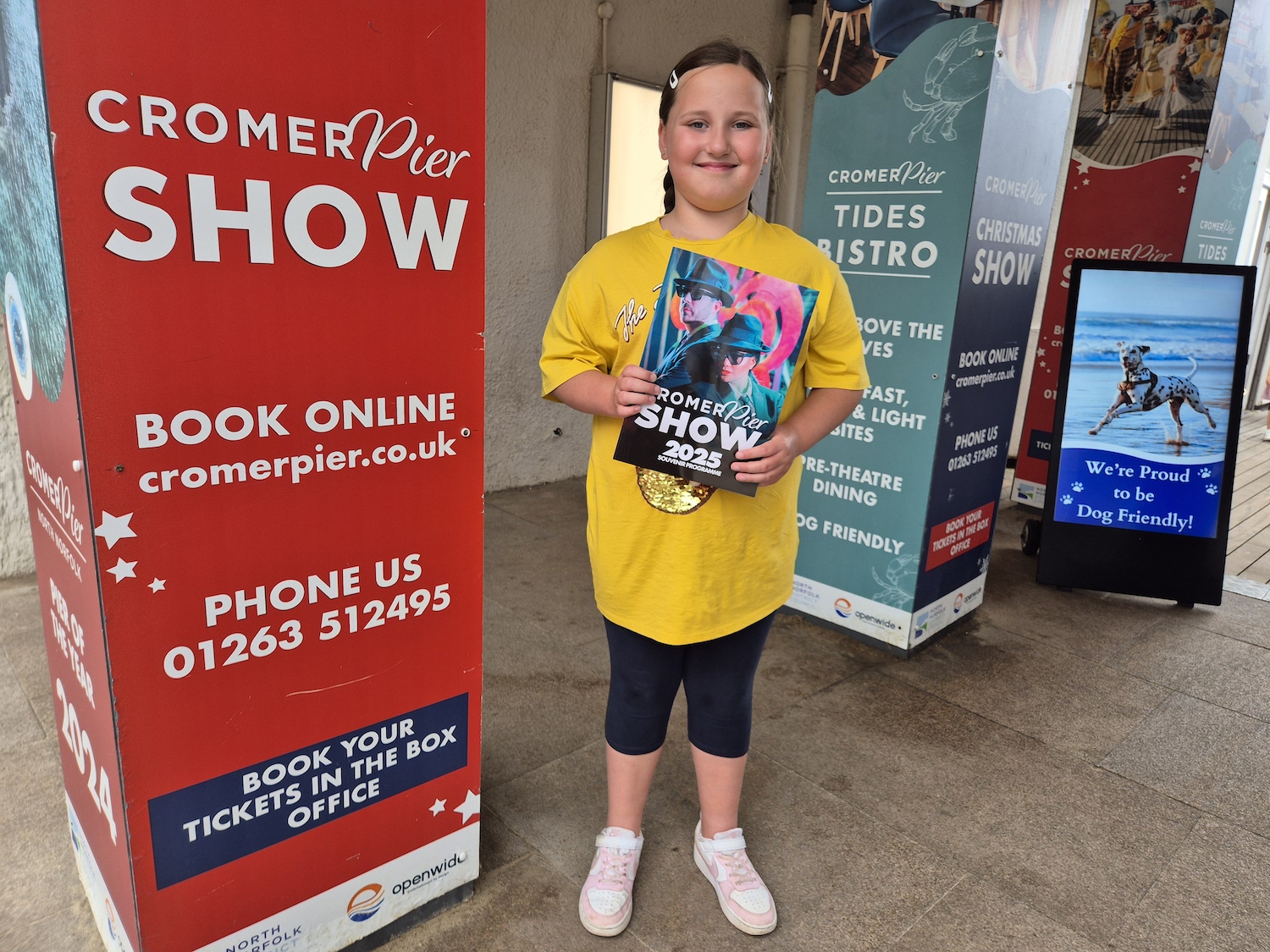 Smiling child holding the Cromer Pier Show 2025 programme next to the box office entrance