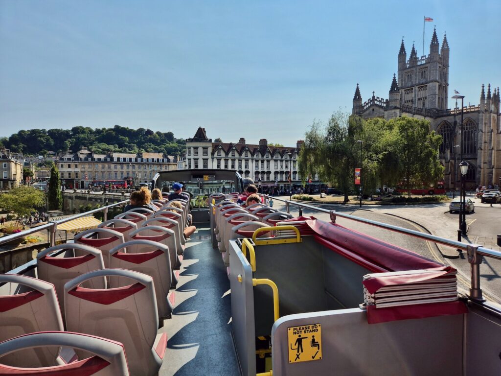 A view from the open-top bus deck showing the city of Bath including Bath Abbey and other buildings.