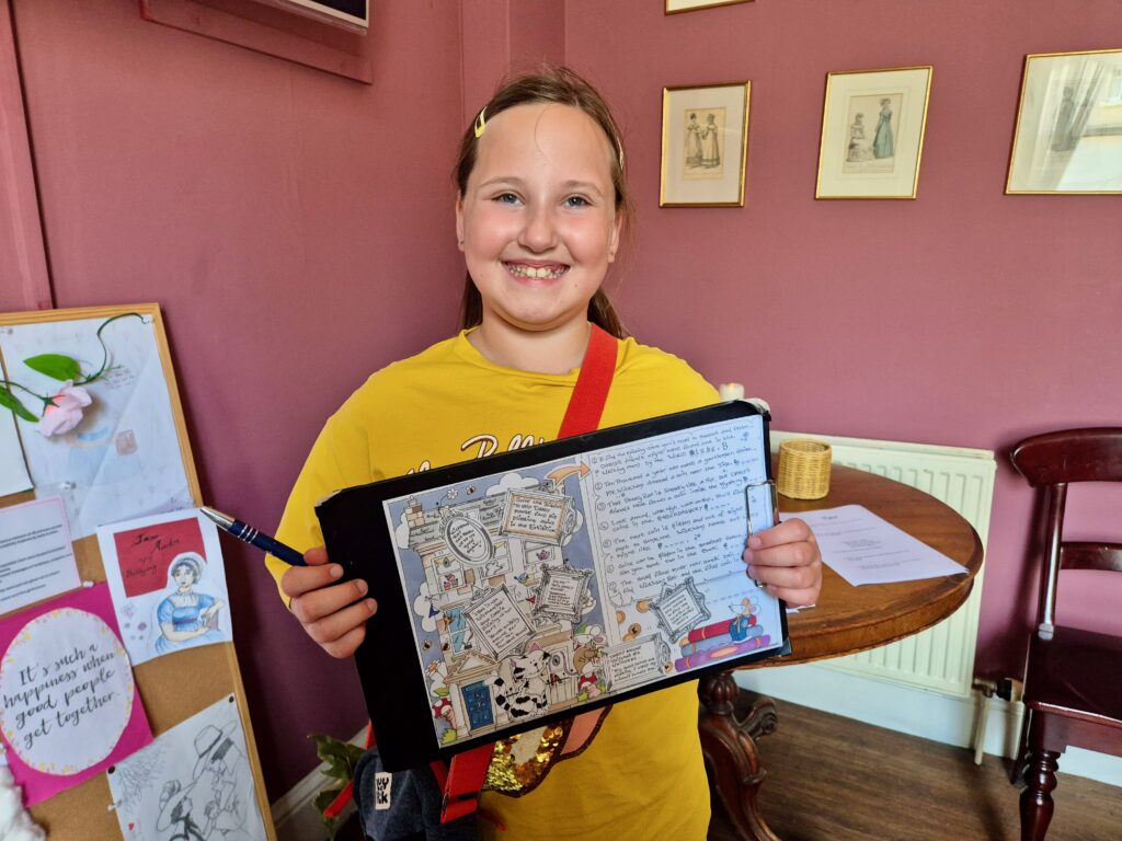 A child smiling while holding a colourful, illustrated activity sheet on a clipboard at the Jane Austen Centre, Bath.