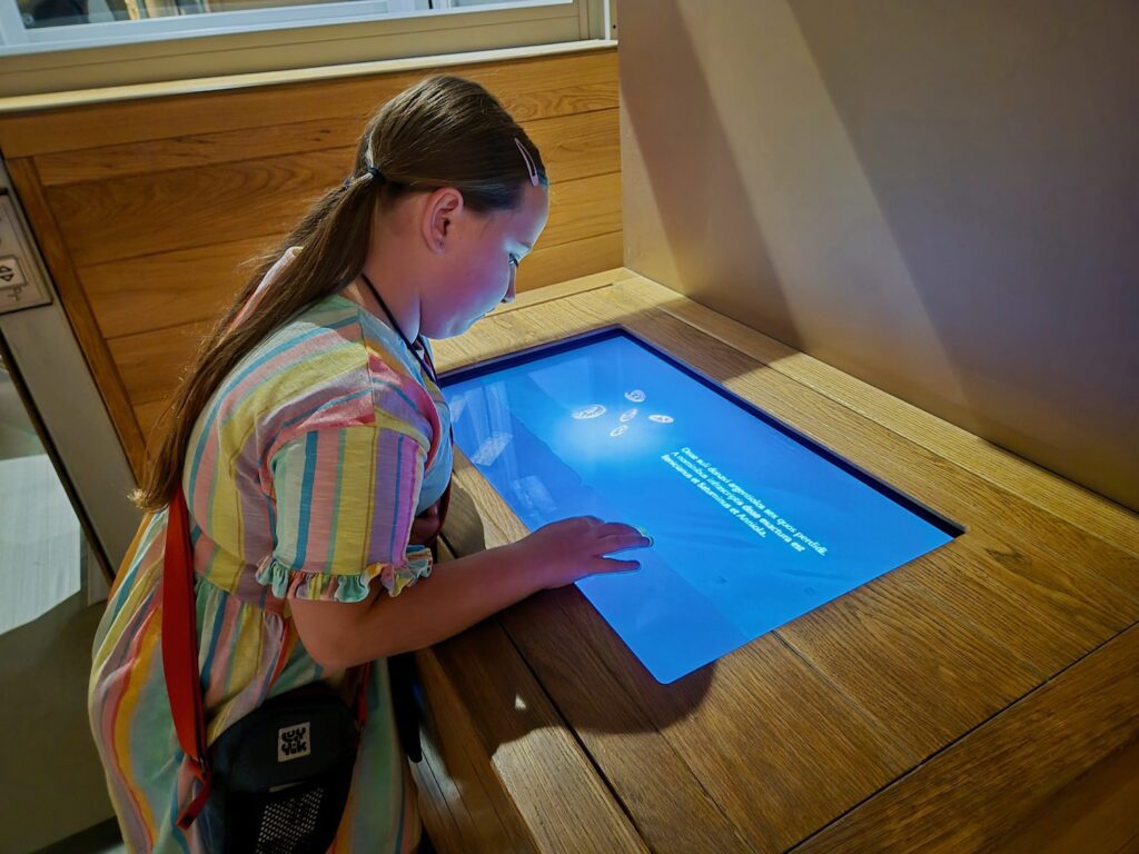 A young girl interacting with a modern touchscreen display at the Roman Baths.