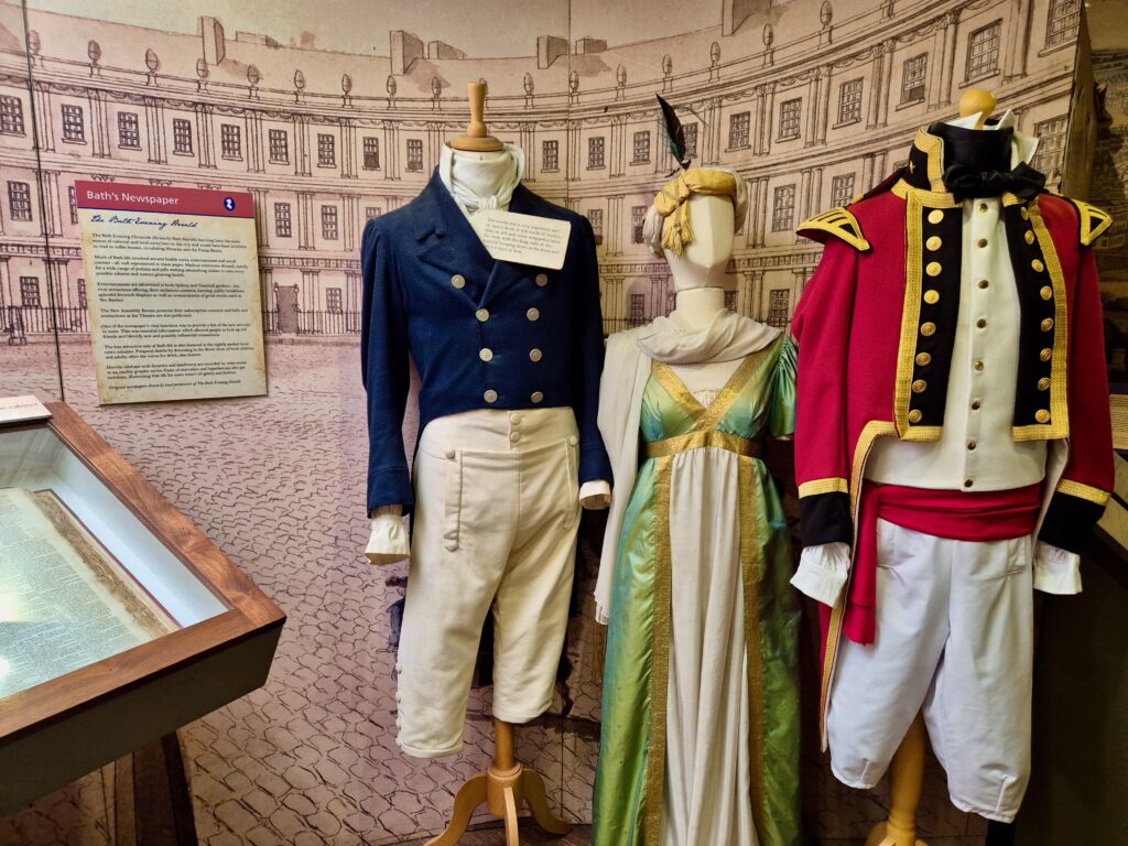 Regency-era costumes including a gentleman’s suit, lady’s gown, and military uniform on display at the Jane Austen Centre in Bath