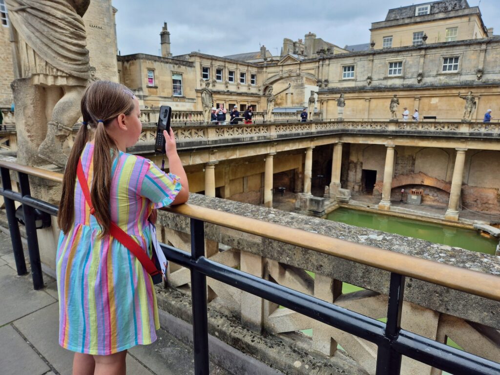 A young girl using an audio guide while looking out at the Roman Baths.